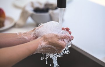 Saippualla vaahdotetut kädet vesihanan alla.