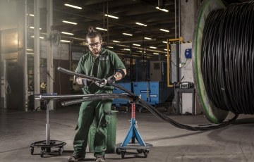 Kaapelityöntekijä testaa kaapelia Rekan Riihimäen tehtaalla, taustalla iso kaapelikela.