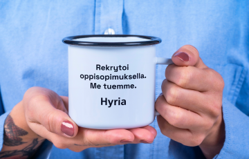 Henkilö pitelee kuppia, jossa teksti "Rekrytoi oppisopimuksella. Me tuemme. Hyria."