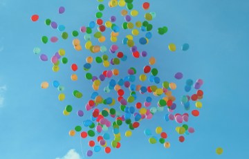 Useita kymmeniä erivärisiä ilmpalloja taivaalla sattumanvaraisessa rykelmässä