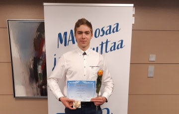 Nuori mies pitelee mitalia ja kunniakirjaa sekä ruusua rollupin edessä.