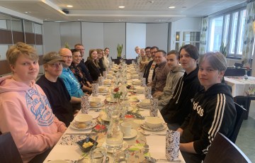 Ihmisiä lounaalla pitkän pöydän ääressä ravintolassa. 