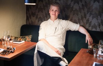 Valokuva jutussa esiintyvästä Aleksista kokkiasu päällään istumassa ravintolapöydän ääressä