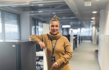 Nainen seisoo käytävälle, hän nojaa kädellään hyllykköön. 