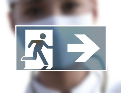 Exit-kyltti jonka takana epätarkat miehen kasvot, miehellä maski kasvoilla.