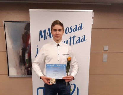 Nuori mies pitelee mitalia ja kunniakirjaa sekä ruusua rollupin edessä.