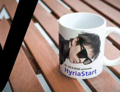 Pöydällä muki, jossa Cledos-artistin kuva ja teksti HyriaStart 21.-22.6.2022 verkossa