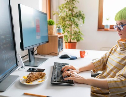 ICT-alantekijä istuu työpöydän ääressä kahden tietokonenäytön edessä ja koodaa.