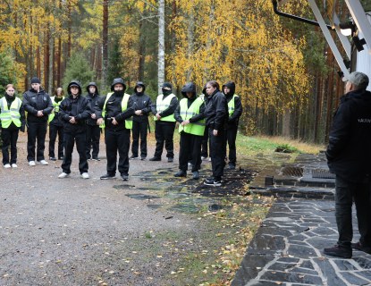 Mustiin haalareihin pukeutuneita ihmisiä ulkona rakennuksen edessä.