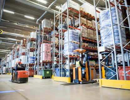 Mies ajaa trukkia korkeiden hyllyjen välissä isossa logistiikkakeskuksessa.