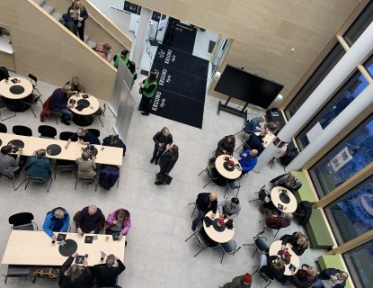 Ylhäältä parvelta katsottuna iso aulatila jossa pöytien ääressä kahvittelee ihmisiä.