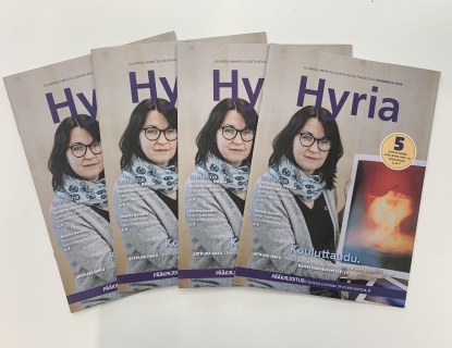 4 Hyria-lehteä viuhkamuodostelmassa pöydällä. Kannes nainen esittelee taidevalokuvaa