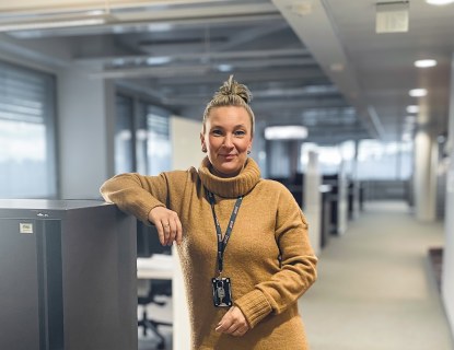 Nainen seisoo käytävälle, hän nojaa kädellään hyllykköön. 