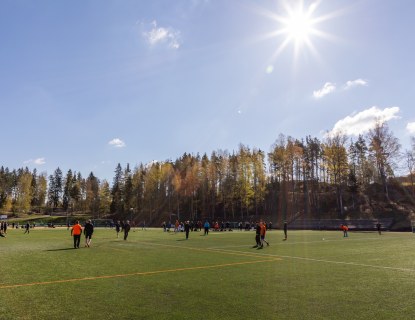 Valokuva jalkapallokentästä. Kentällä on pelaajia ja aurinko paistaa.
