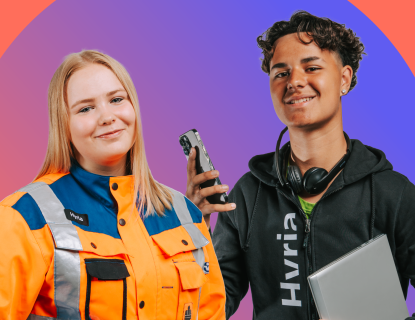 Tyttö huomiovärisessä työasussa, vieressä poika, jolla puhelin ja kannettava tietokone